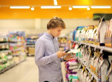 Man shopping in supermarket reading product information.Using smarthone.Pet food