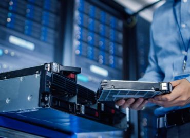 In the Modern Data Center: IT Engineer is Holding New HDD Hard Drive Prepared for Installing Hardware Equipment into Server Rack. IT Specialist Doing Maintenance and Updating Hardware.