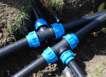 Black three way plastic water pipe on grass. Irrigation system in the garden concept